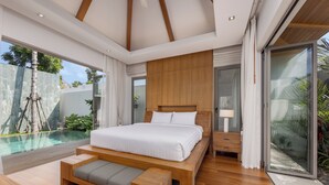 A modern bedroom with a large bed, a wooden bench, a nightstand, and a glass door leading to a pool area. - Modern 3BR Villa Kaimana Private Pool (Thep Krasattri)