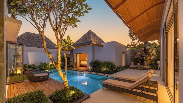 A modern outdoor pool area with lounge chairs, a wooden deck, and a glass-enclosed room. - Modern 3BR Villa Kaimana Private Pool (Thep Krasattri)