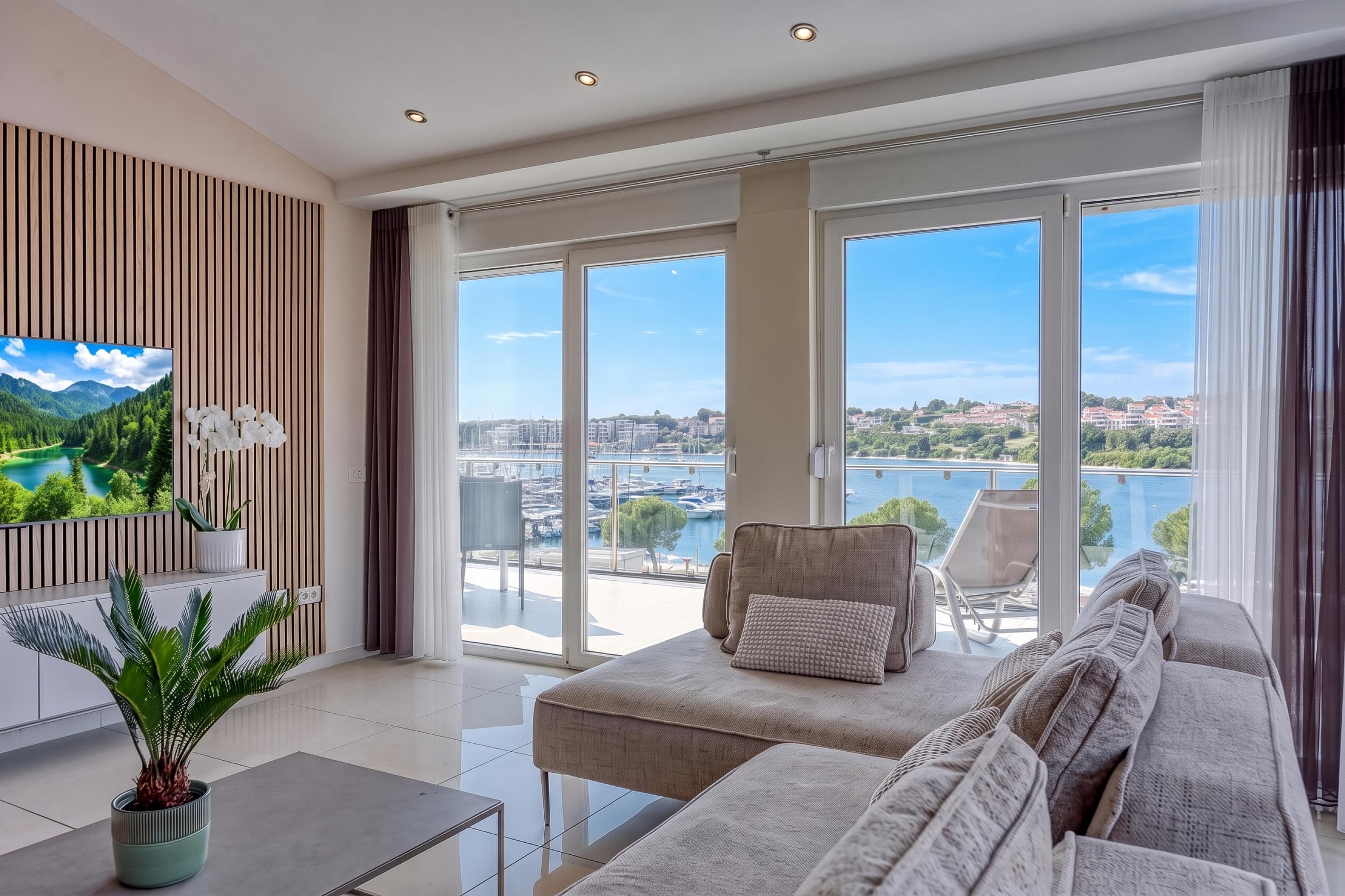 A modern living room with a sofa, chairs, a TV, and a view of a marina and water.