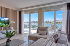 A modern living room with a sofa, chairs, a TV, and a view of a marina and water. - Elegant Panoramic Seaview Apartments (Medulin)