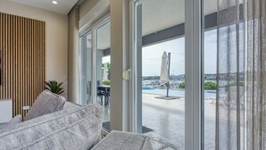 Ett modernt vardagsrum med en soffa, en matplats och utsikt över en småbåtshamn genom stora glasdörrar.