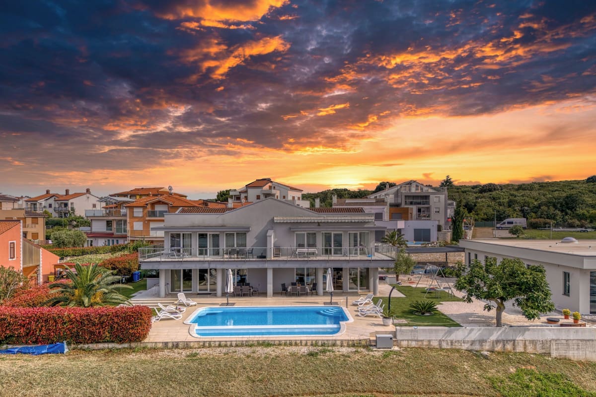 A modern house with a swimming pool, surrounded by greenery and other houses.