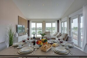 A dining area with a table set for a meal, a sofa, and large windows with a view. - Elegant Panoramic Seaview Apartments (Medulin)
