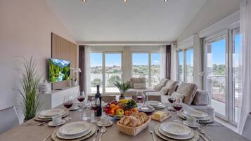 Comedor con mesa dispuesta para seis personas, televisor en la pared y vistas al exterior.