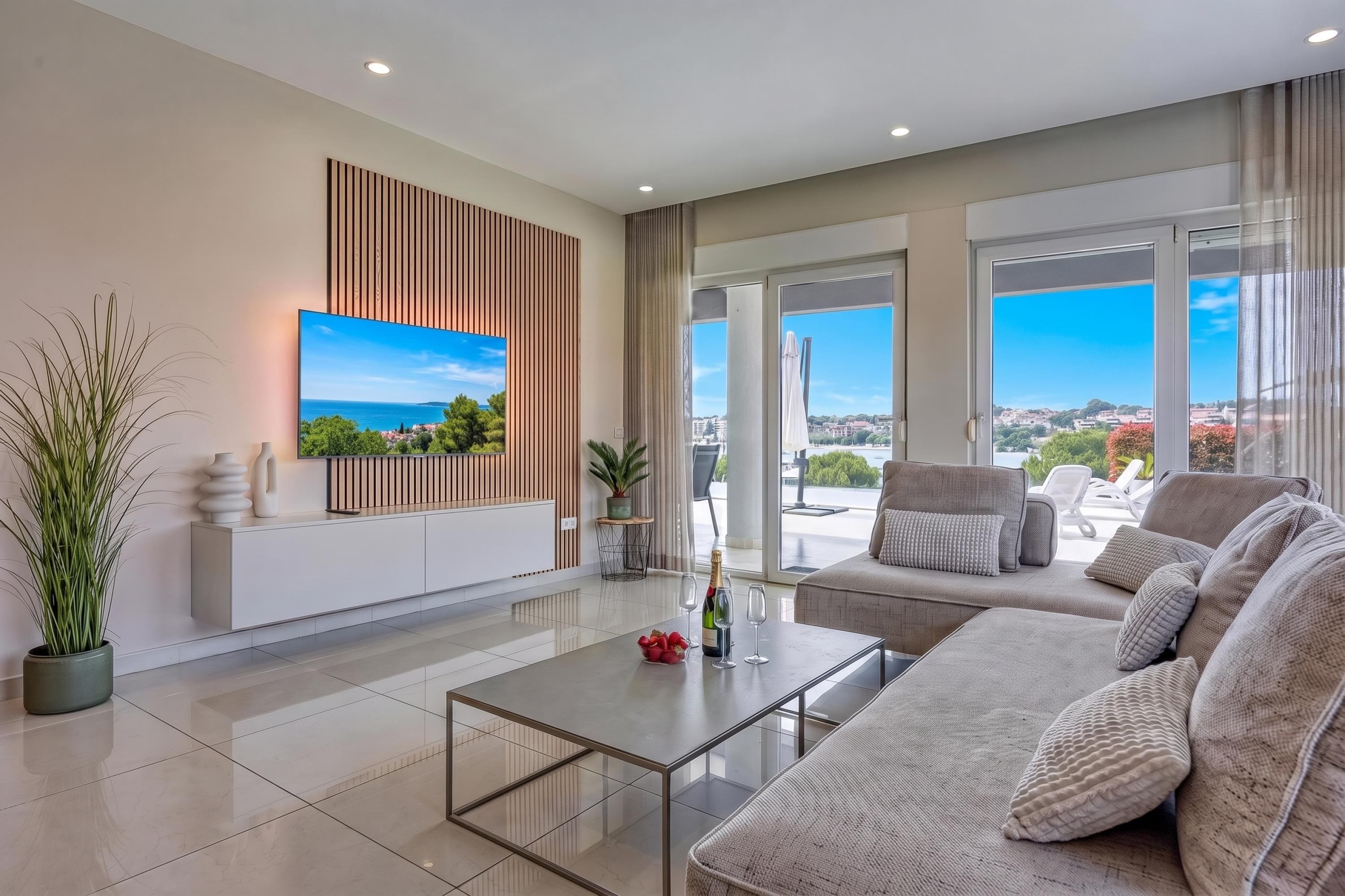 Una sala de estar moderna con una televisión de pantalla plana, un sofá, una mesa de centro y vista al mar a través de amplios ventanales.