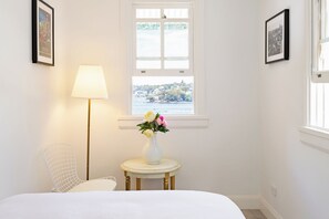 A room with a bed, a lamp, a vase with flowers, a chair, and a window with a view.