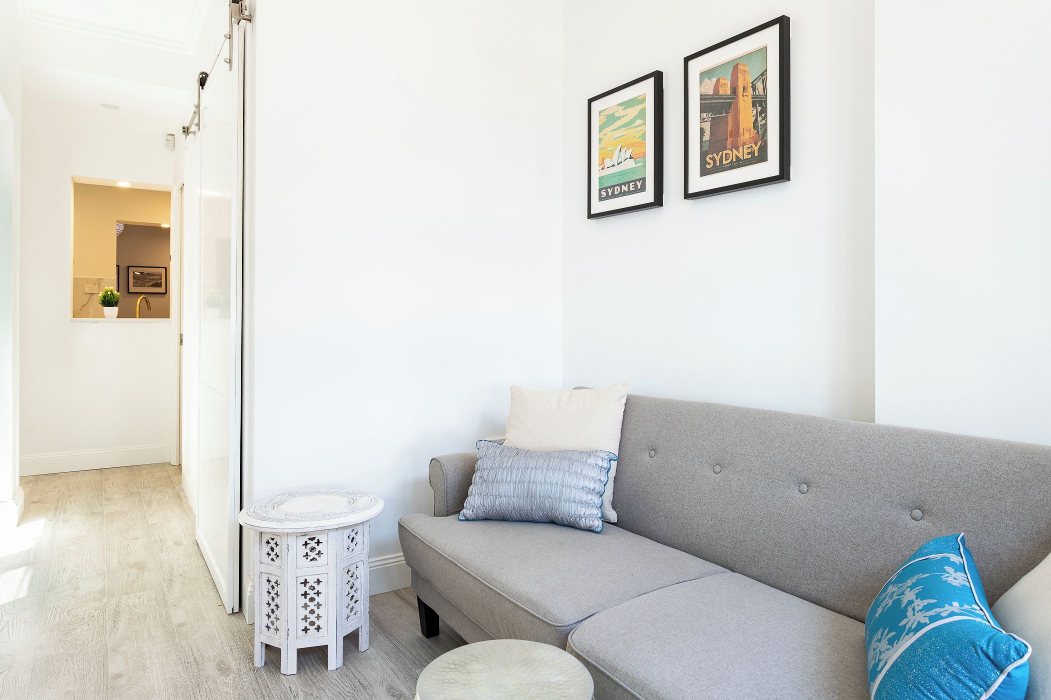 A modern living room with a grey sofa, a small round table, and two framed pictures on the wall.