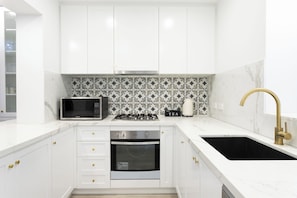 Une cuisine moderne avec des meubles blancs, un four à micro-ondes, une cuisinière à gaz, un four et un évier noir avec un robinet doré.