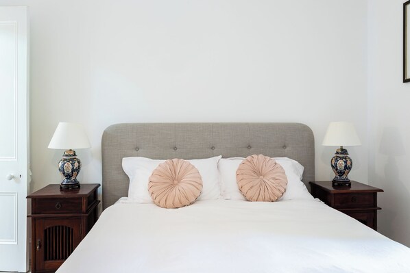 A neatly made bed with a grey upholstered headboard, two bedside tables with lamps, and a white door.