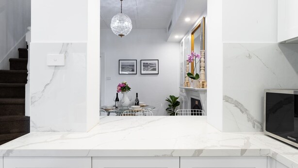 Uma cozinha moderna com bancadas de mármore, uma área de jantar com mesa redonda e uma TV à direita.
