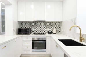 Una cocina moderna con armarios blancos, microondas, estufa a gas, horno y un lavamanos negro con grifo dorado.