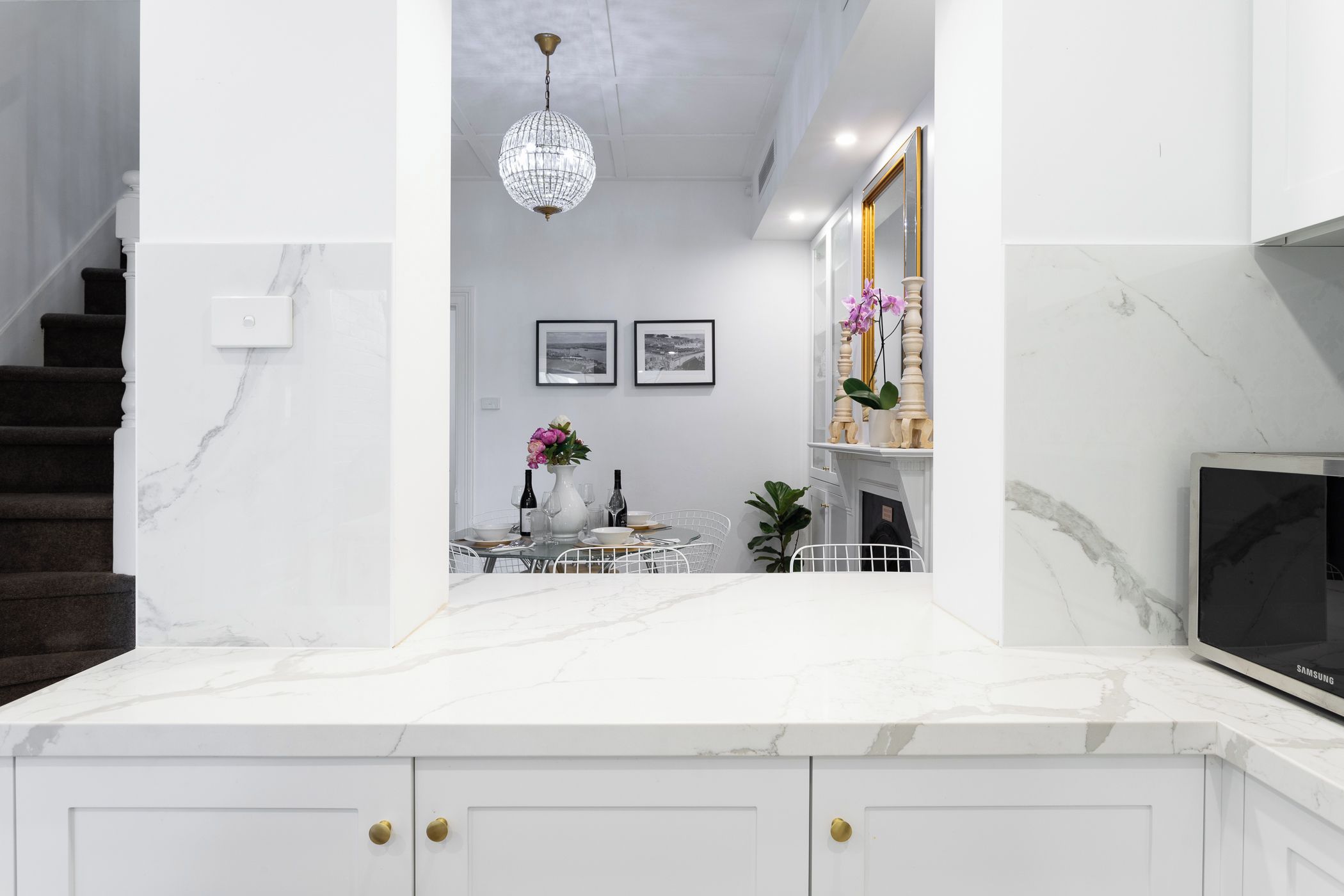 Een moderne keuken met witte kasten, een marmeren aanrecht, een eethoek met een tafel voor twee personen en een grote flatscreen-televisie.