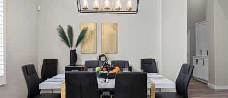 Un comedor con una mesa rectangular, sillas tapizadas en negro, una araña y dos paneles decorativos en la pared.