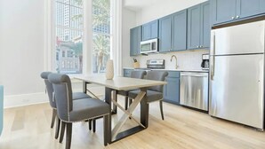 Eine moderne Küche mit blauen Schränken, einem Edelstahlkühlschrank und einem Essbereich mit Holztisch und -stühlen.