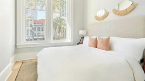 Ein Hotelzimmer mit einem großen Bett, Blick auf eine Stadtkulisse durch ein Fenster und zwei an der Wand befestigte Spiegel.