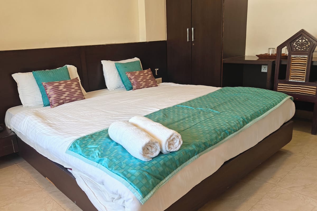 A neatly made bed with a green and white bedspread, two rolled towels, and multiple pillows in various patterns.