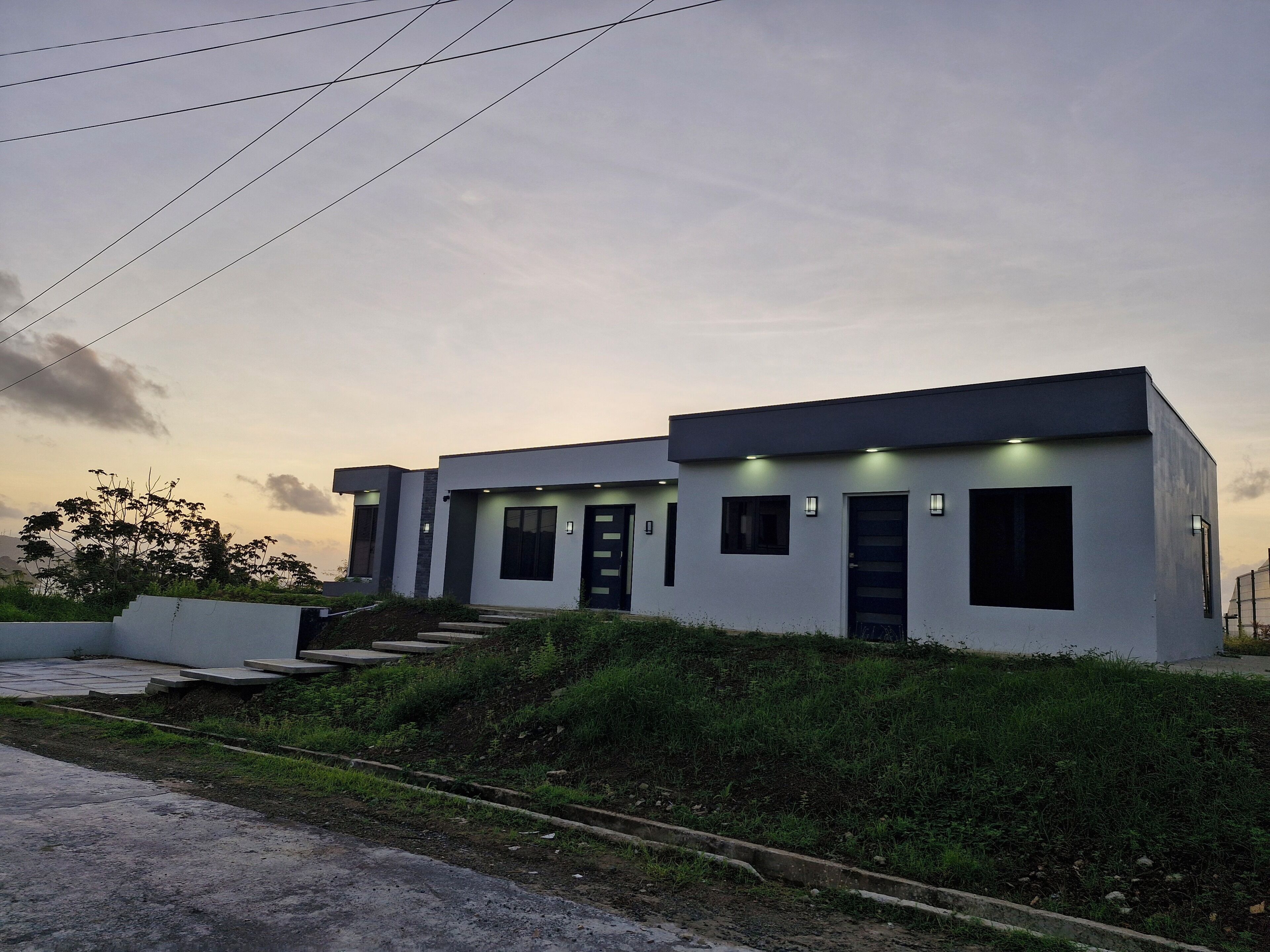 Una casa moderna de dos pisos con techo plano, ventanas amplias y un pequeño porche delantero.