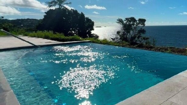 Une piscine à l’eau d’un bleu cristallin, entourée d’une terrasse en béton et d’une végétation luxuriante.