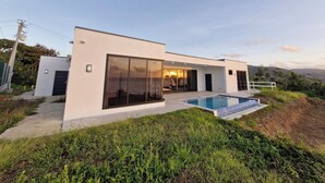 Una casa moderna de dos pisos con amplias puertas correderas de vidrio, una piscina y vista al océano.