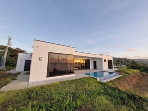 A modern two-story house with large sliding glass doors, a swimming pool, and a view of the ocean. - Panoramic seascape from modern, 3-bedroom villa in Hope Estate (Mesopotamia)