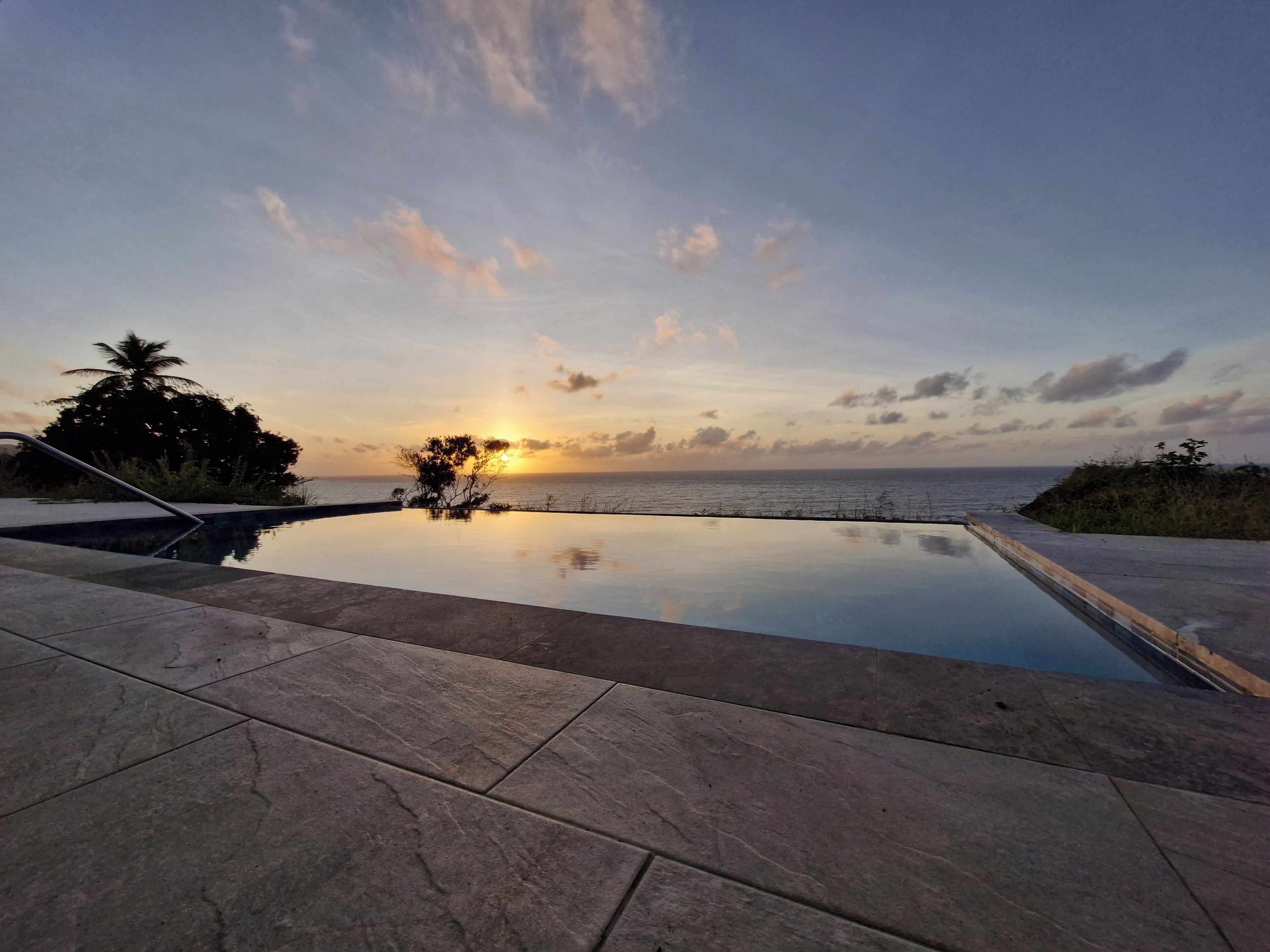 An infinity pool with a view of the sunset over the ocean.