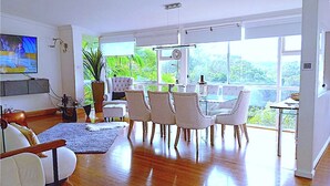 A spacious living room with a large dining table, comfortable seating, a TV, and a view of greenery outside. - Grand Haven with Sea view! For Executives and Remote! Adults only! City Close! (Castlecrag)
