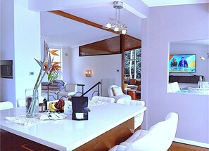Ein modernes Wohnzimmer mit einer weißen Sofagarnitur, einem Essbereich mit weißem Tisch und einem an der Wand befestigten Fernseher.