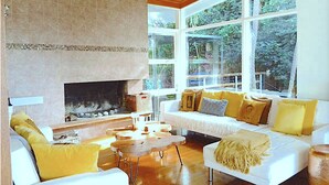 A cozy living room with a fireplace, large windows, and a white sofa with yellow cushions. - Grand Haven with Sea view! For Executives and Remote! Adults only! City Close! (Castlecrag)