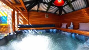 A hot tub with wooden walls and a metal roof, surrounded by wooden benches and cushions.
