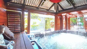 A hot tub area with a wooden deck, a Buddha statue, and a view of greenery outside.