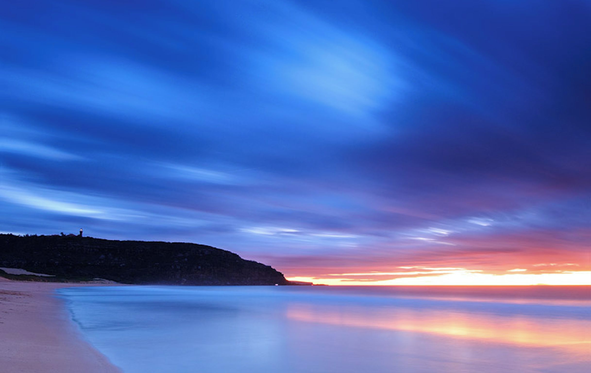 A beach with a calm sea and a sunset sky.