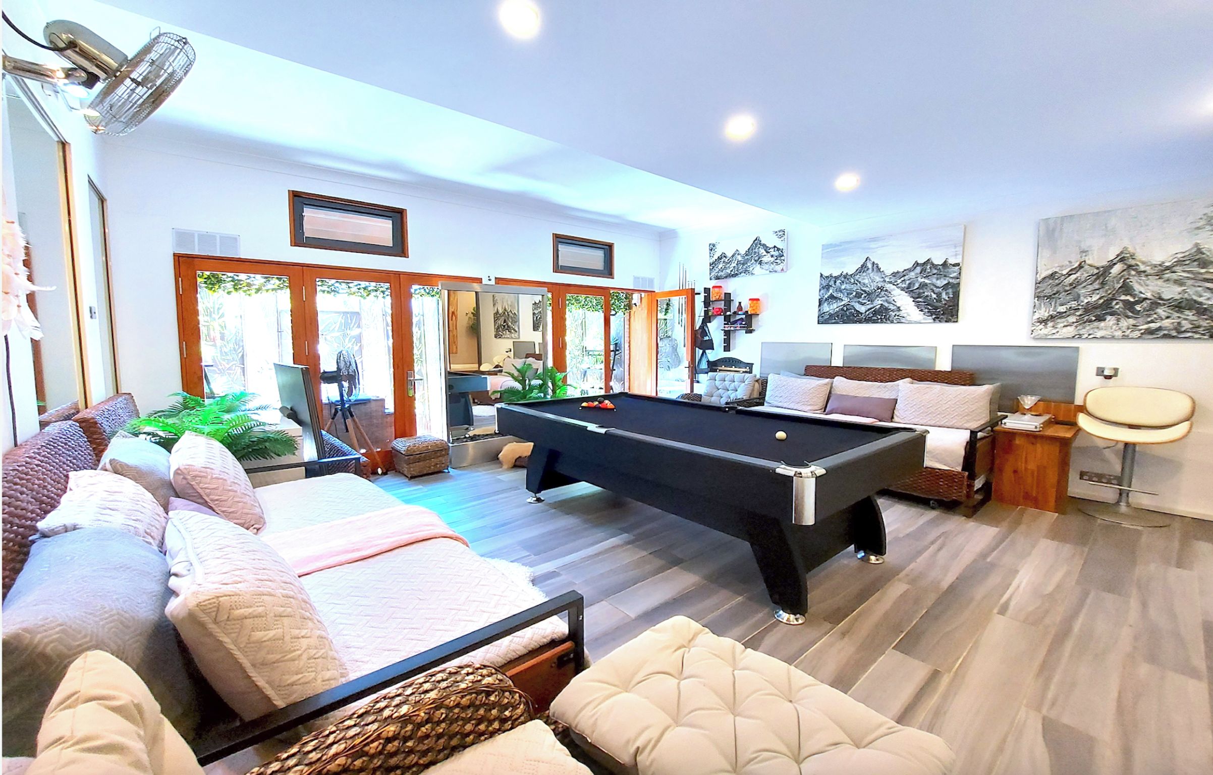 Una sala de estar moderna con mesa de billar, asientos cómodos y vistas a un área exterior a través de puertas de vidrio.