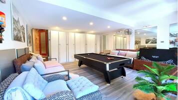A modern living room with a pool table, comfortable seating, and a large mirror.