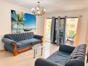 Una sala de estar con un sofá azul, una mesa de centro de vidrio y un cuadro de una playa.