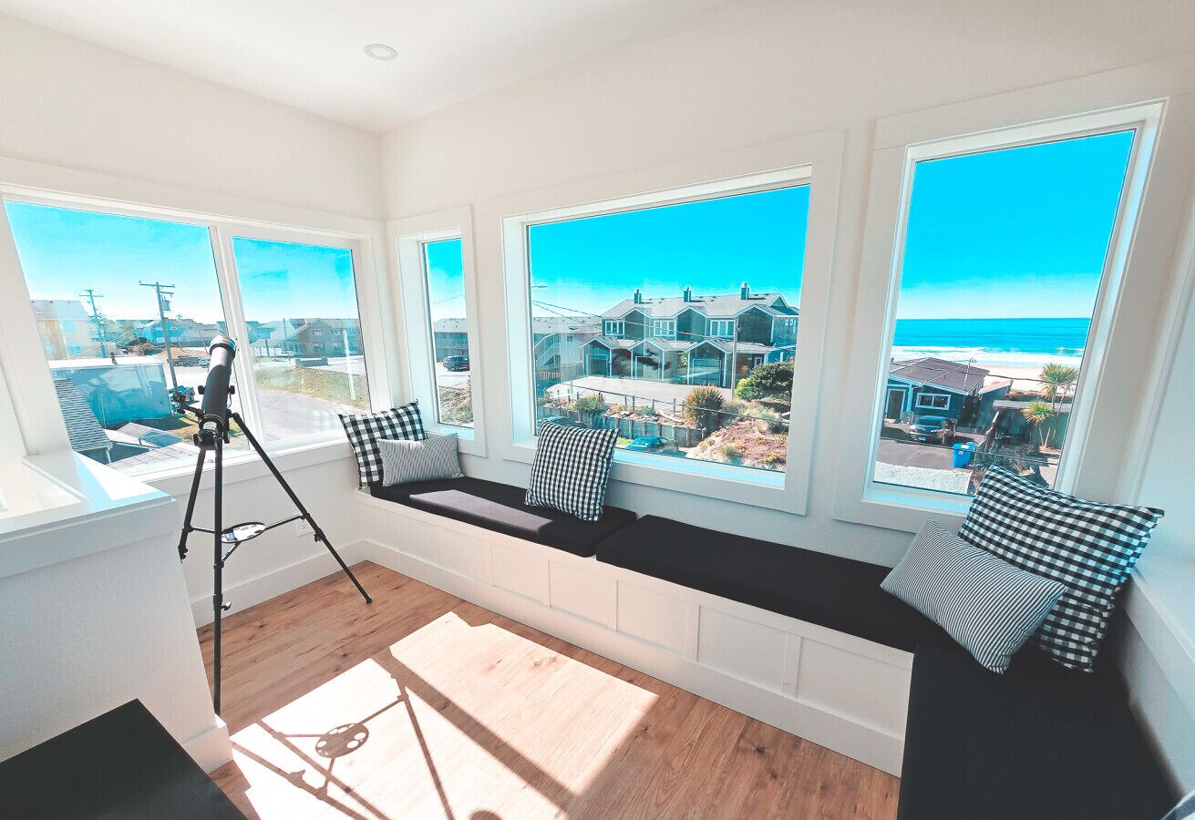A room with large windows, a bench with cushions, and a tripod.
