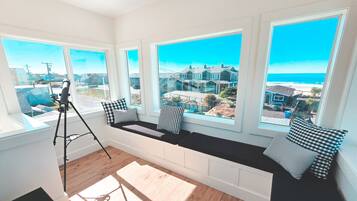 A room with large windows, a bench with cushions, and a tripod.