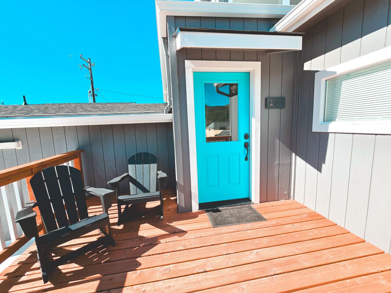 A wooden deck with a turquoise door, a small porch area, and a chair.