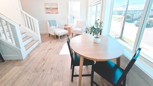 Ein heller, offener Wohnbereich mit einer Holztreppe, einem runden Esstisch mit Stühlen, einem Blumentopf und großen Fenstern mit Blick ins Freie.