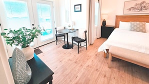 Et hotelværelse med en seng, et skrivebord med stol, en potteplante og et vindue med skodder.