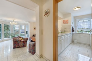 A spacious living area with a sofa, a dining table, and a kitchen with white cabinets and a window. - Apartment 'Linas Lieblingsplatz' with Balcony & Piano (Uhldingen-Mühlhofen)