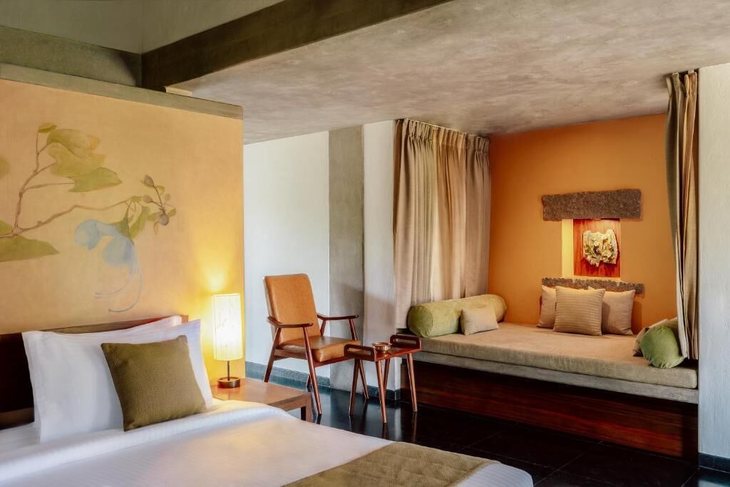 A hotel room with a bed, a chair, a sofa, a lamp, and a painting on the wall.