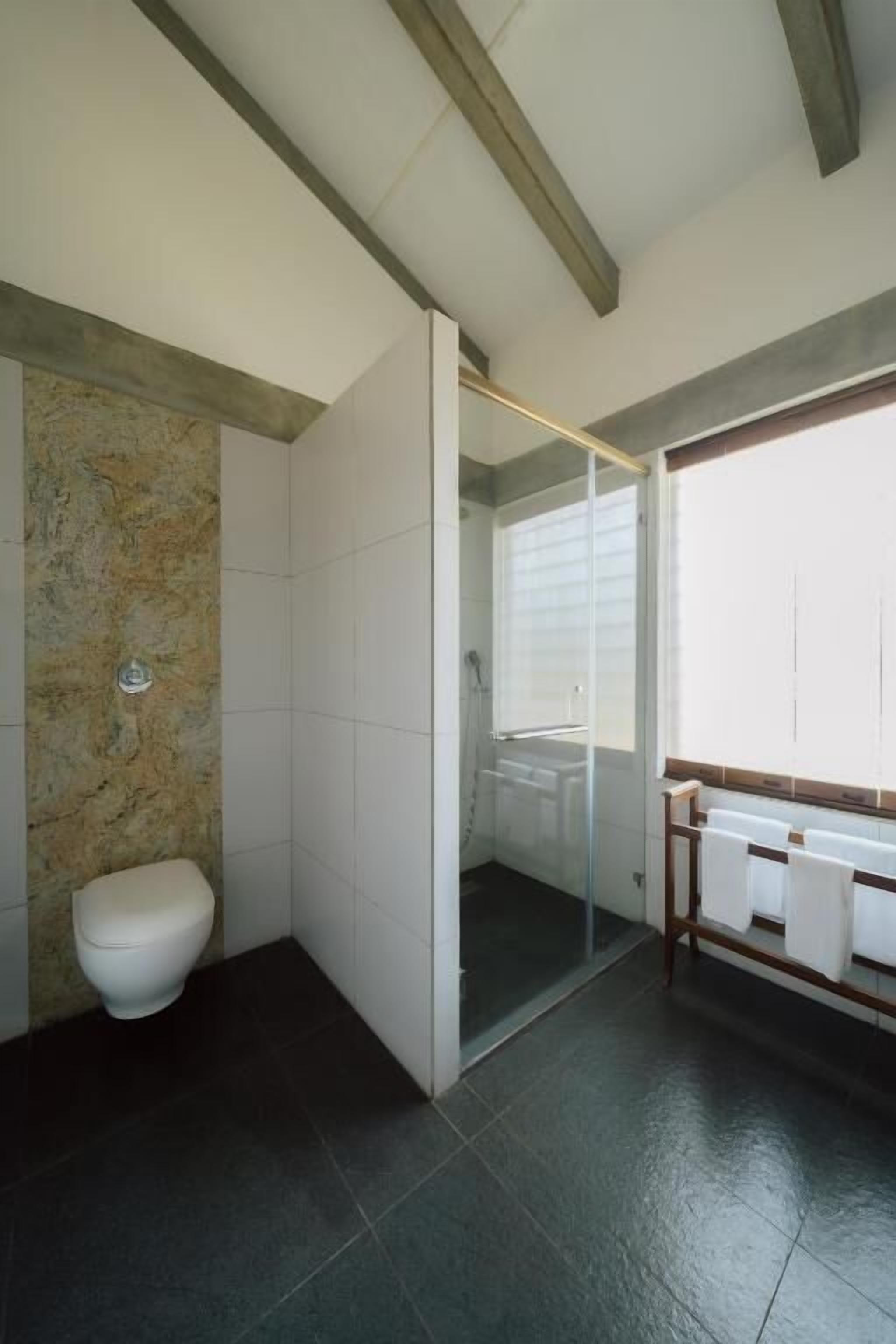 A modern bathroom with a stone accent wall, a glass shower enclosure, and a wooden vanity with towels.