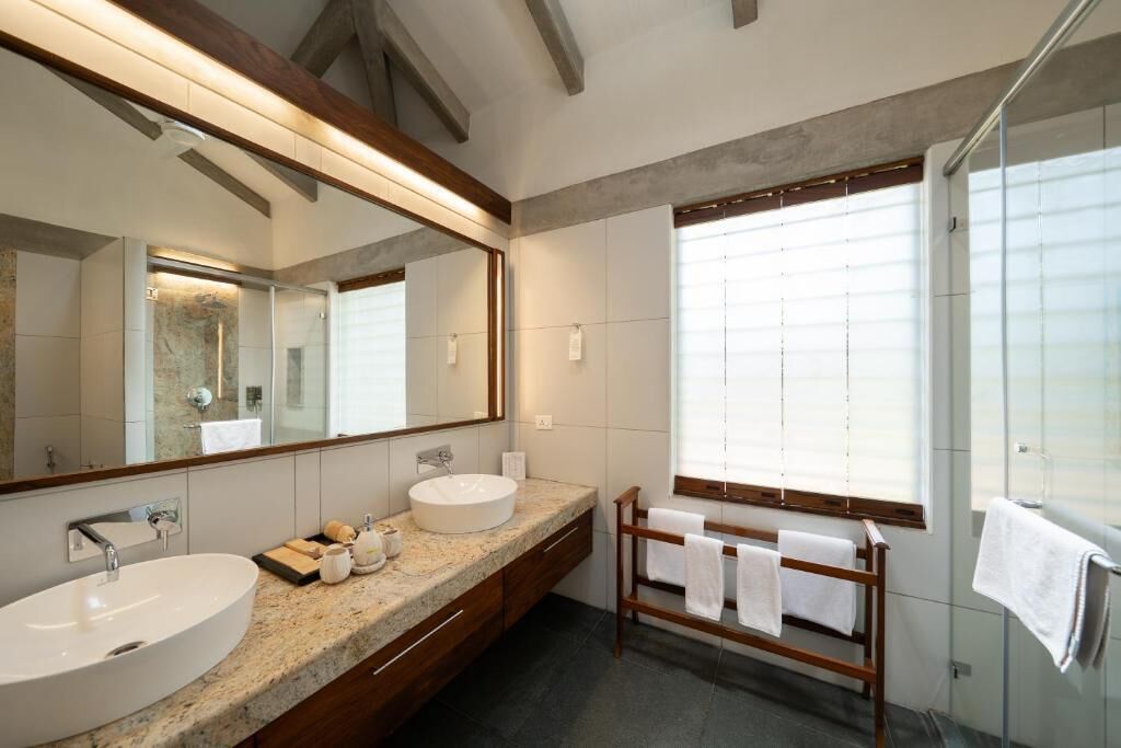A modern bathroom with a large mirror, a sink, a vanity, a wooden towel rack, and a glass shower enclosure.