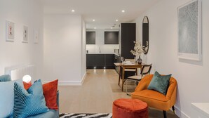 Ein modernes Wohnzimmer mit einer Couch, einem Hocker und einem Essbereich mit Tisch und Stühlen.