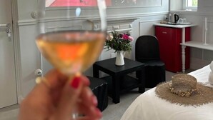 A hotel room with a bed, a small table with a vase of flowers, a red cabinet, and a large screen displaying a sports event. - Maison LYO - "Lys" Romantic Luxury Suite (Cannes)