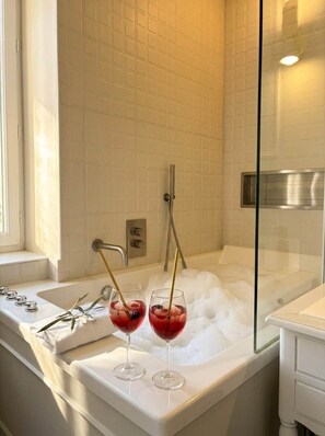 A bathroom with a bathtub, a window, and two glasses of red liquid on the counter. - Lily (Cannes)