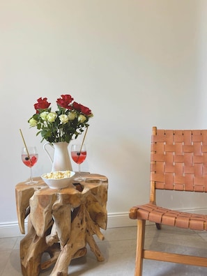 A wooden table with a vase of flowers and two glasses of red liquid, a bowl of popcorn, and a woven chair. - Olivier (Cannes)