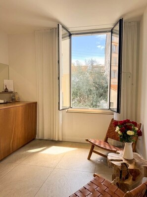 A room with a wooden desk, a chair, a small table with a vase, and a window with curtains. - Olivier (Cannes)