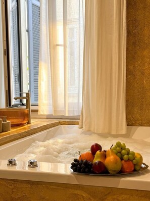 Una bañera con arreglos de frutas, una ventana con persianas y un perchero para toallas.