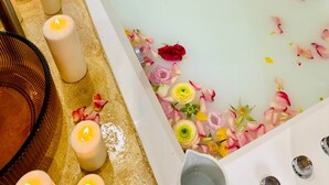 En kvinna i ett badkar fyllt med vatten och rosenblad, omgiven av ljus och blommor.